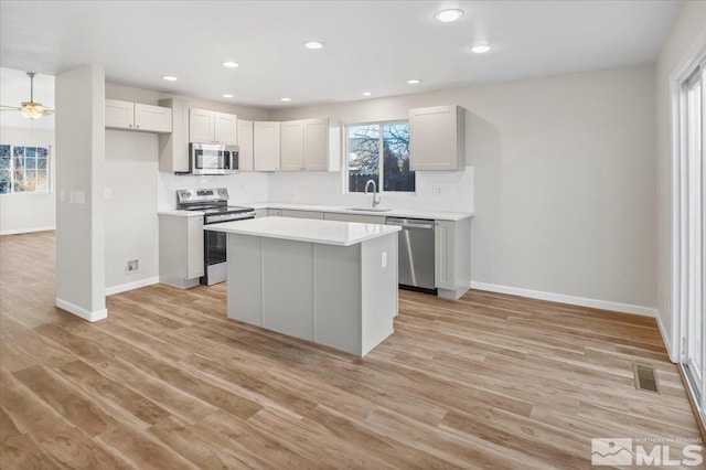 kitchen with appliances with stainless steel finishes, a center island, white cabinets, light hardwood / wood-style flooring, and sink