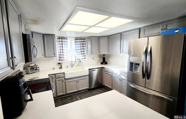 kitchen featuring appliances with stainless steel finishes, gray cabinetry, a textured ceiling, and sink