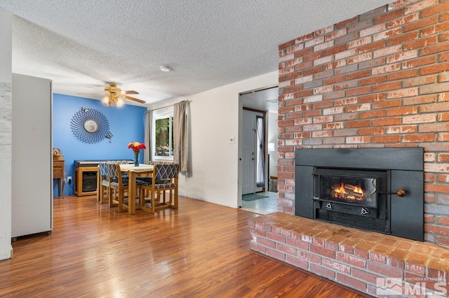 living room with a large fireplace, hardwood / wood-style flooring, a textured ceiling, and ceiling fan