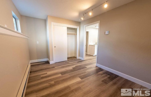 unfurnished bedroom with baseboard heating, a closet, and hardwood / wood-style floors