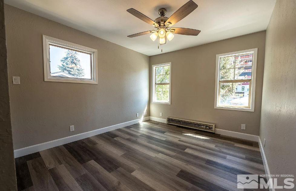 empty room with ceiling fan, dark hardwood / wood-style flooring, a wealth of natural light, and a baseboard heating unit