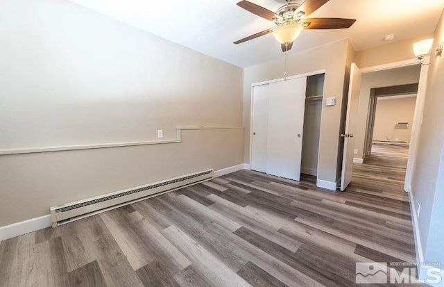 unfurnished bedroom featuring ceiling fan, baseboard heating, dark hardwood / wood-style flooring, and a closet