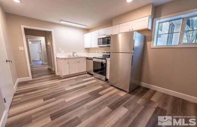 kitchen featuring stainless steel appliances, white cabinets, wood-type flooring, and sink