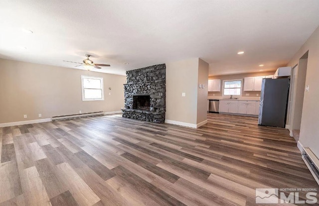 unfurnished living room featuring baseboard heating, hardwood / wood-style flooring, a fireplace, and plenty of natural light