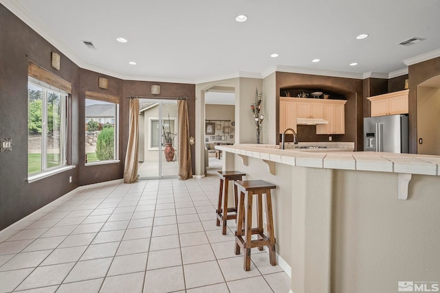 kitchen featuring a kitchen bar, tile counters, high quality fridge, and ornamental molding