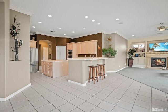 kitchen featuring light carpet, stainless steel appliances, an island with sink, ornamental molding, and a kitchen bar