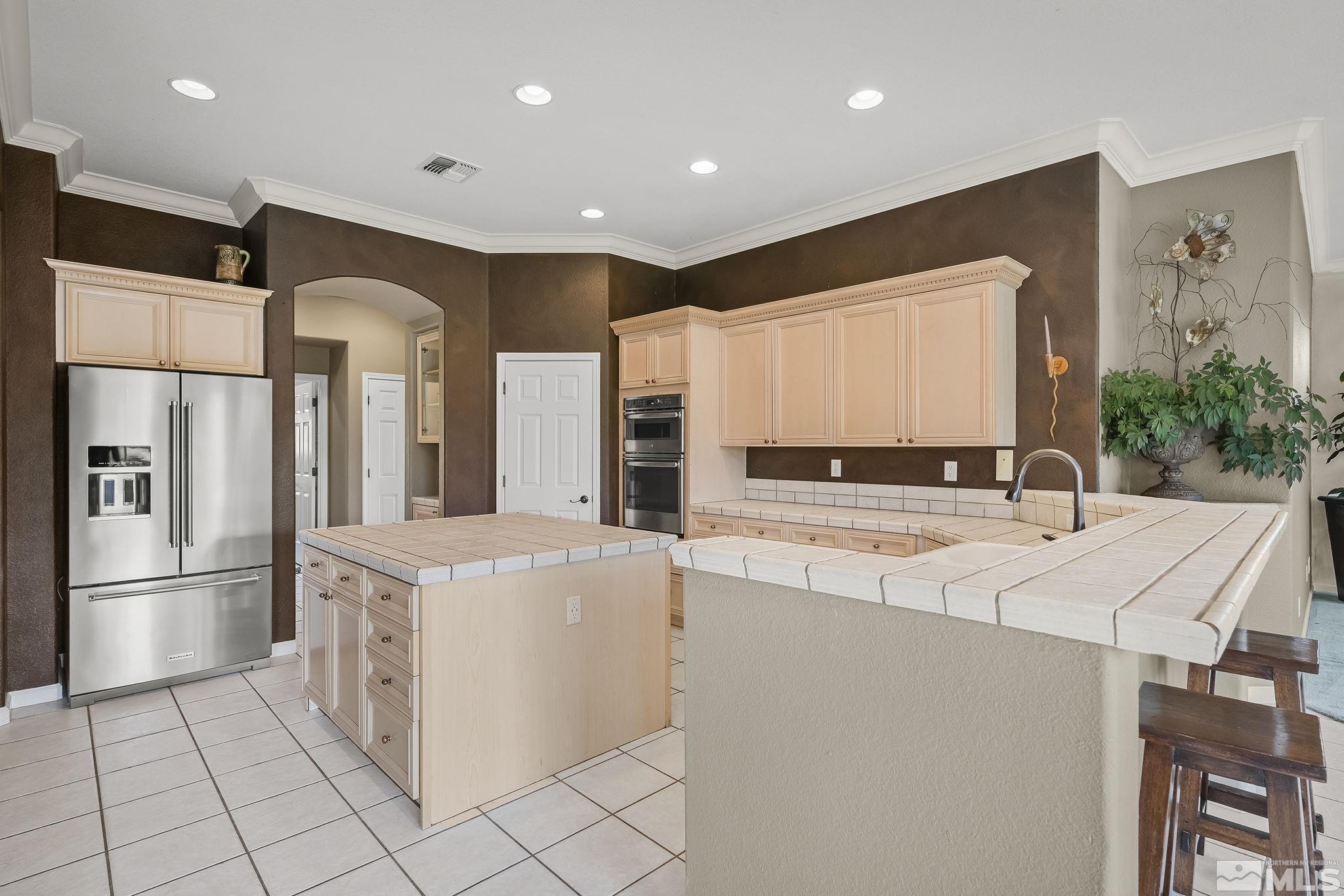 kitchen with stainless steel appliances, tile countertops, light tile patterned flooring, kitchen peninsula, and crown molding