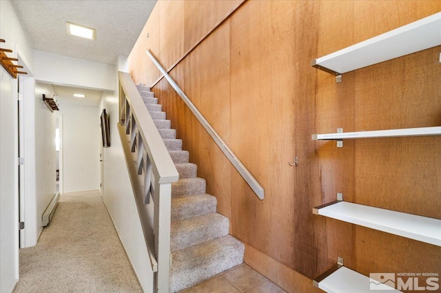 stairs with a baseboard heating unit, a textured ceiling, and wood walls