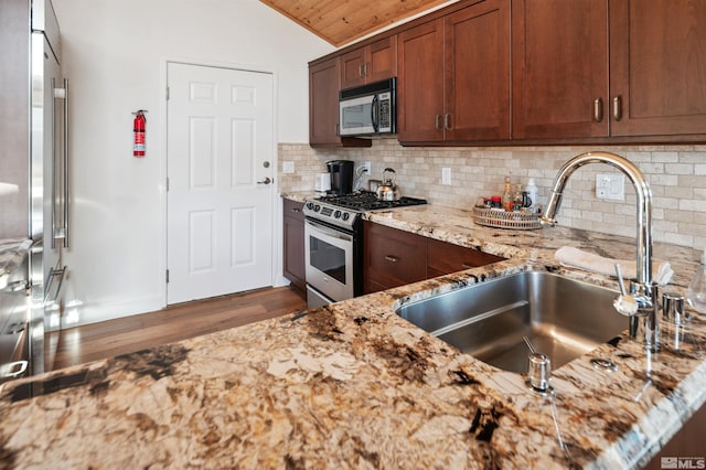 kitchen with wooden ceiling, appliances with stainless steel finishes, light stone counters, sink, and tasteful backsplash