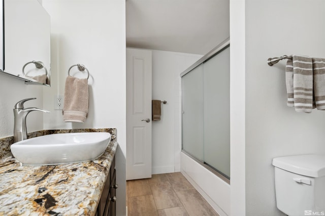 full bathroom with combined bath / shower with glass door, vanity, and toilet