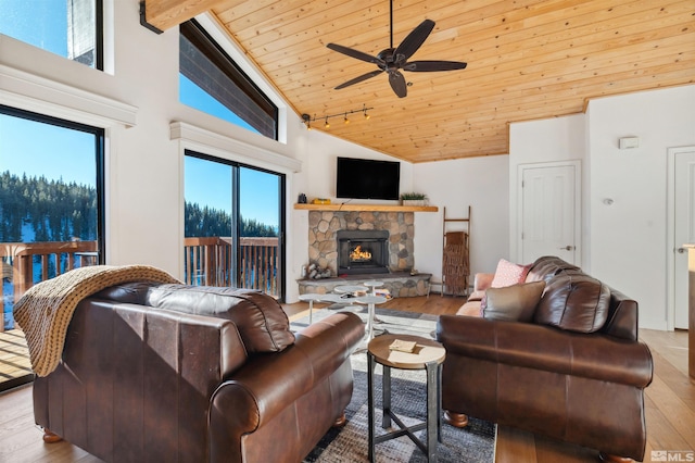 living room featuring wood ceiling, a stone fireplace, light wood-type flooring, ceiling fan, and beam ceiling