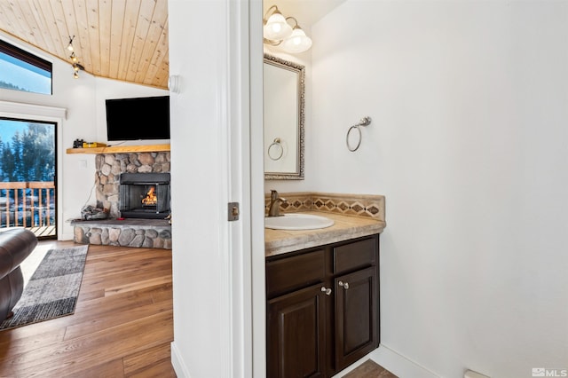 bathroom with vaulted ceiling, hardwood / wood-style floors, vanity, wood ceiling, and a stone fireplace