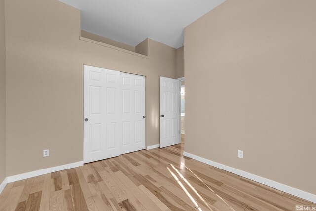 unfurnished bedroom with a high ceiling, a closet, and light hardwood / wood-style flooring