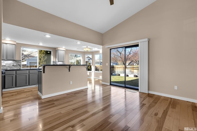 kitchen featuring high vaulted ceiling, light hardwood / wood-style floors, gray cabinetry, and a kitchen breakfast bar