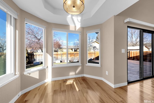 unfurnished dining area featuring a raised ceiling, light hardwood / wood-style flooring, and plenty of natural light