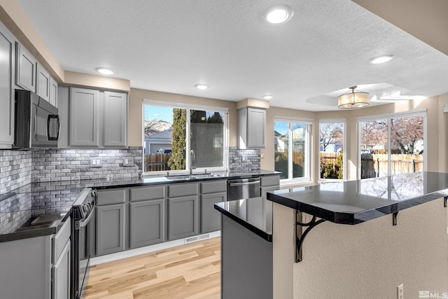 kitchen featuring sink, backsplash, a breakfast bar, gray cabinetry, and appliances with stainless steel finishes