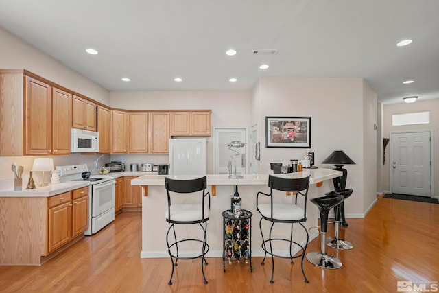 kitchen with white appliances, light wood-type flooring, a center island, a breakfast bar, and light brown cabinets