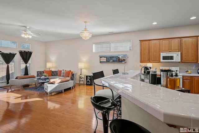 kitchen with white appliances, tile counters, hanging light fixtures, light wood-type flooring, and ceiling fan with notable chandelier