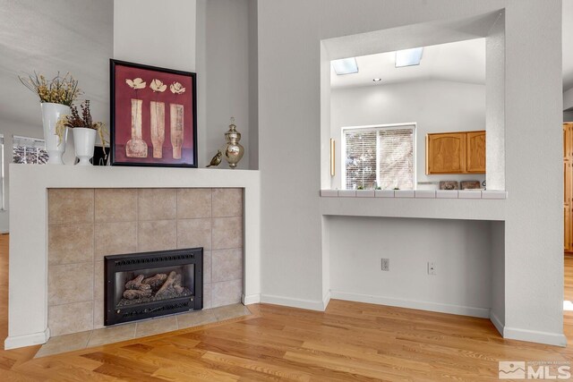 living room with light hardwood / wood-style floors, a tile fireplace, and lofted ceiling