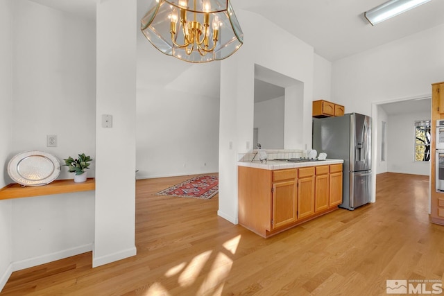 kitchen with decorative light fixtures, gas cooktop, light hardwood / wood-style floors, stainless steel refrigerator with ice dispenser, and a notable chandelier