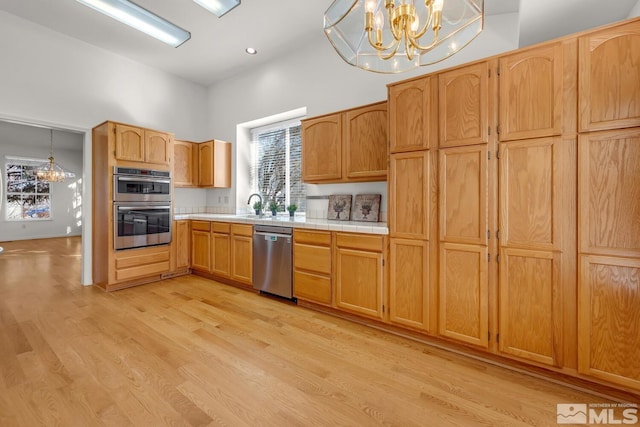 kitchen with tile counters, light hardwood / wood-style flooring, decorative light fixtures, stainless steel appliances, and an inviting chandelier