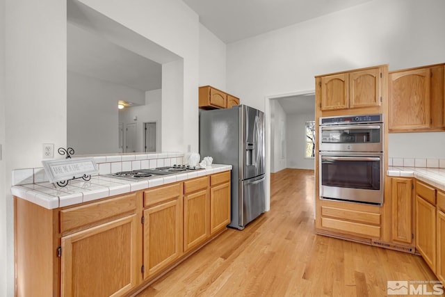 kitchen with stainless steel appliances, light wood-type flooring, and tile counters