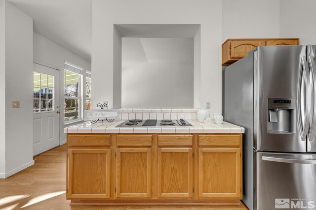 kitchen featuring stainless steel fridge with ice dispenser, light wood-type flooring, electric stovetop, and tile counters