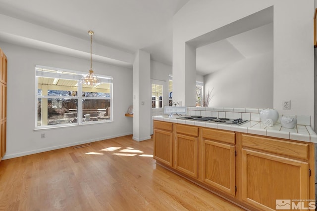 kitchen with tile counters, an inviting chandelier, stainless steel gas cooktop, and a wealth of natural light