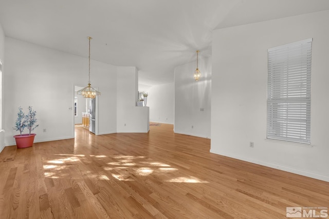 unfurnished living room with a notable chandelier, light hardwood / wood-style flooring, and lofted ceiling