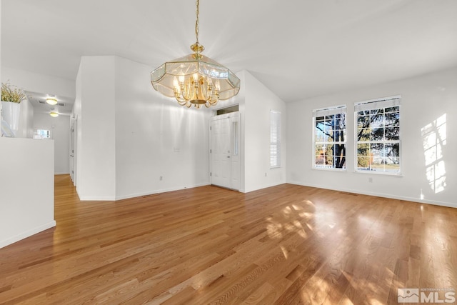 unfurnished living room featuring hardwood / wood-style floors, a chandelier, and vaulted ceiling