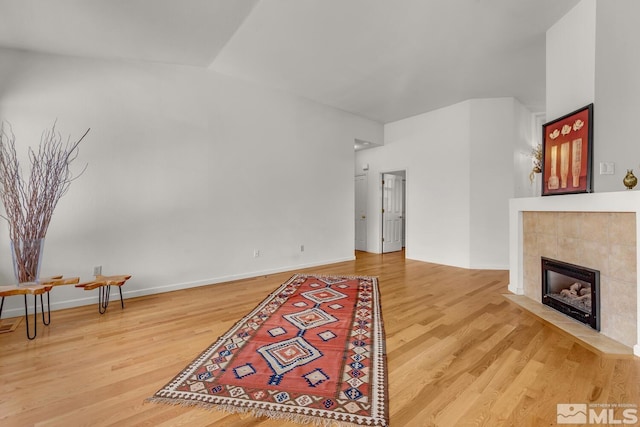 living room with a tile fireplace, vaulted ceiling, and hardwood / wood-style flooring