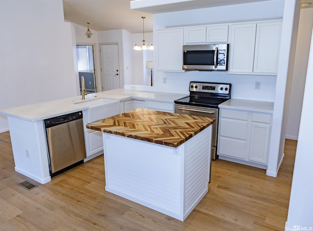 kitchen featuring stainless steel appliances, white cabinets, an inviting chandelier, decorative light fixtures, and kitchen peninsula