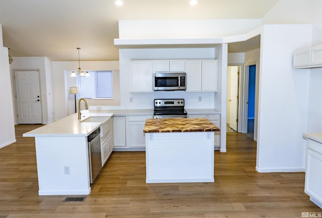 kitchen featuring stainless steel appliances, sink, white cabinets, decorative light fixtures, and a kitchen island