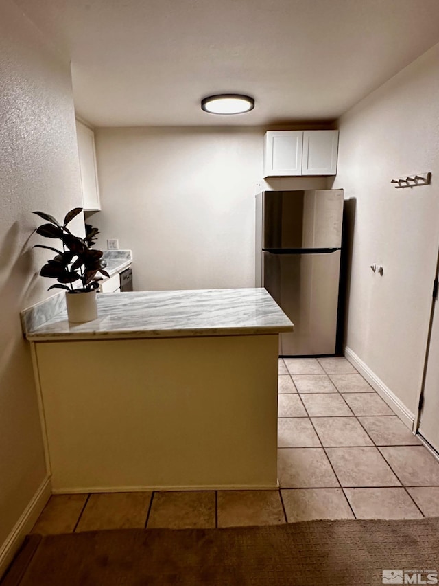 kitchen featuring white cabinets, light tile patterned flooring, stainless steel refrigerator, and kitchen peninsula