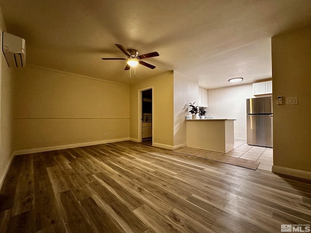 unfurnished living room featuring a wall unit AC, wood-type flooring, and ceiling fan