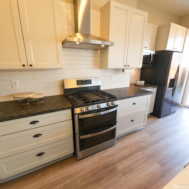 kitchen featuring stainless steel appliances, wall chimney range hood, light wood-type flooring, white cabinets, and dark stone countertops