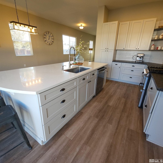 kitchen with appliances with stainless steel finishes, hanging light fixtures, white cabinets, and a center island with sink