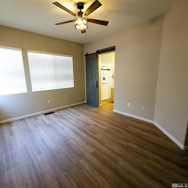 unfurnished room with ceiling fan, a barn door, and dark hardwood / wood-style floors