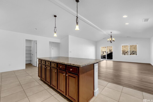 kitchen featuring a chandelier, a center island, light stone countertops, light tile patterned floors, and pendant lighting