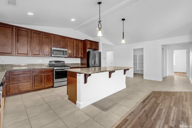 kitchen featuring decorative light fixtures, stone counters, a breakfast bar area, a kitchen island, and appliances with stainless steel finishes