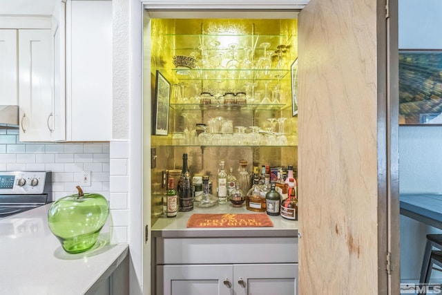 bar featuring stainless steel electric range, white cabinetry, and decorative backsplash