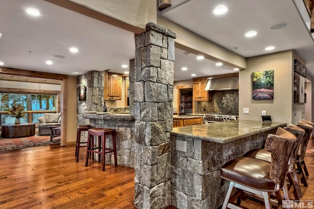 bar featuring decorative columns, wall chimney exhaust hood, hardwood / wood-style floors, decorative backsplash, and range