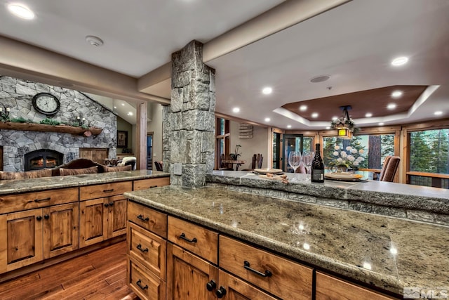 kitchen featuring light stone counters, dark wood-type flooring, vaulted ceiling, and a stone fireplace