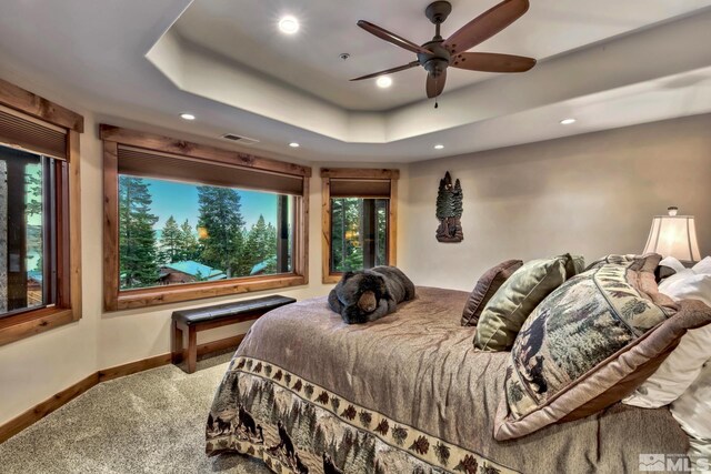 carpeted bedroom with ceiling fan and a tray ceiling