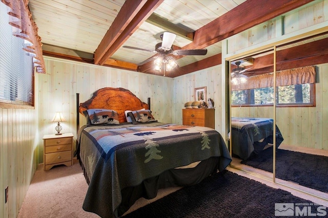 carpeted bedroom featuring wooden walls, a closet, ceiling fan, and beam ceiling