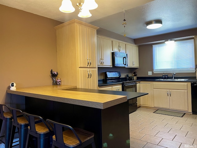 kitchen featuring sink, a textured ceiling, a kitchen bar, kitchen peninsula, and black appliances