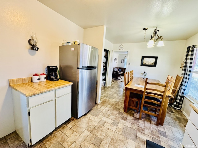 kitchen featuring white cabinets, stainless steel refrigerator, pendant lighting, and a notable chandelier