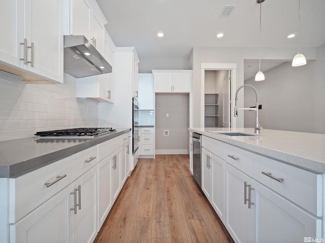 kitchen with appliances with stainless steel finishes, hanging light fixtures, wall chimney exhaust hood, white cabinets, and sink