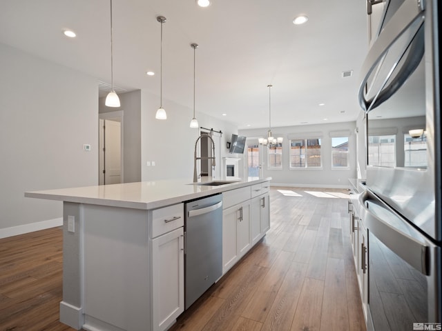 kitchen with a kitchen island with sink, white cabinets, decorative light fixtures, stainless steel dishwasher, and sink