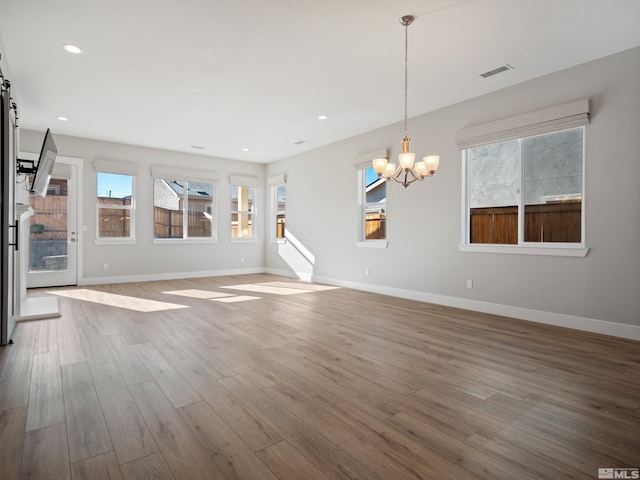 unfurnished living room with a healthy amount of sunlight, hardwood / wood-style floors, a barn door, and a chandelier